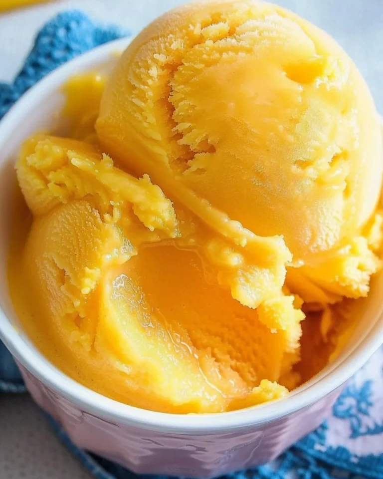A bowl of vibrant mango sorbet topped with mint leaves, served on a wooden table.